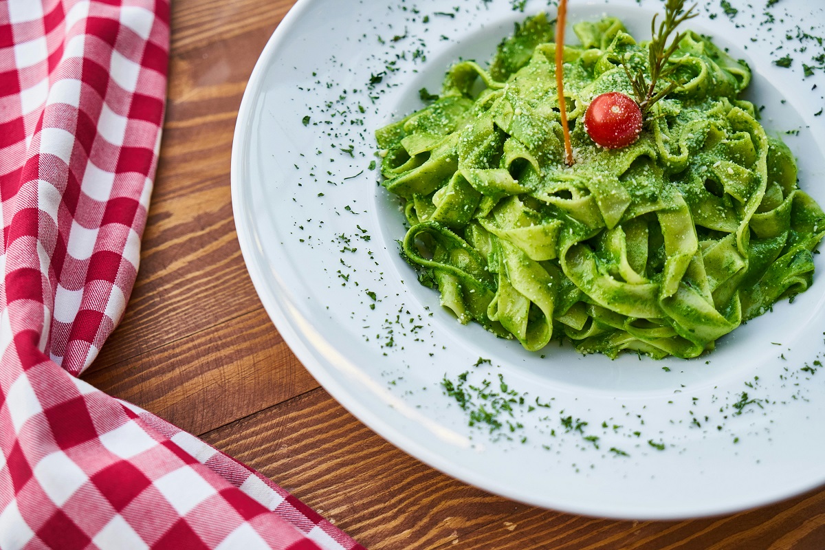 pesto pasta with a cherry tomato on top and a red gingham table napkin 